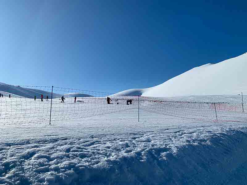 Pista de ski de Corralco, no Chile, com pessoas esquiando ao fundo e céu azul