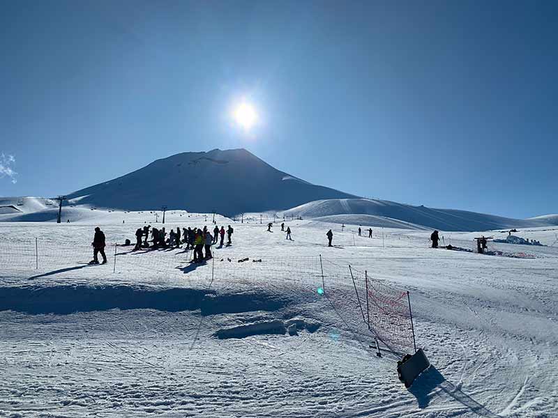 Sol no fim de tarde em centro de ski com pessoas na pista com neve