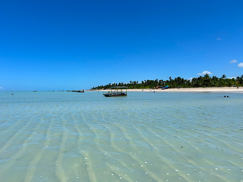 Mar cristalino com barco ao fundo na Praia de Antunes em dia de céu azul