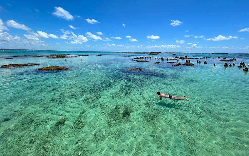 Homem mergulha nas piscinas naturais, dica de o que fazer em Maragogi, em dia de céu azul com poucas nuvens