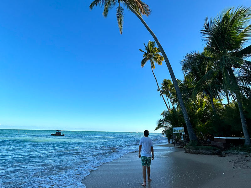 Homem caminha nas areias da Ponta do Mangue, dica de o que fazer em Maragogi, ao lado de coqueiros