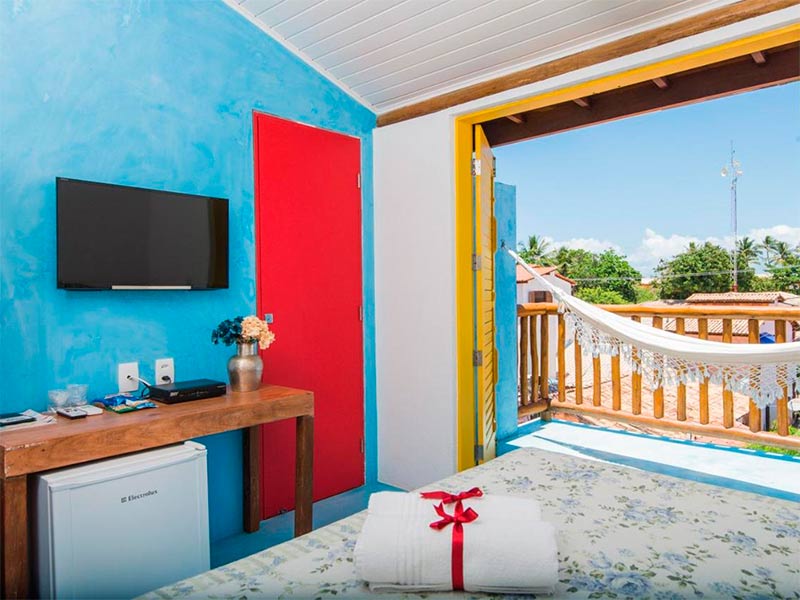 Quarto da Rosa dos Ventos com cama de casal, varanda com rede, TV e parede azul