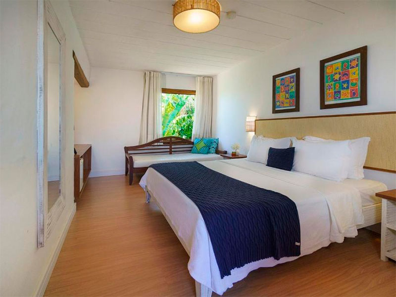 Quarto da Vila dos Corais com cama de casal, piso de madeira e quadros coloridos