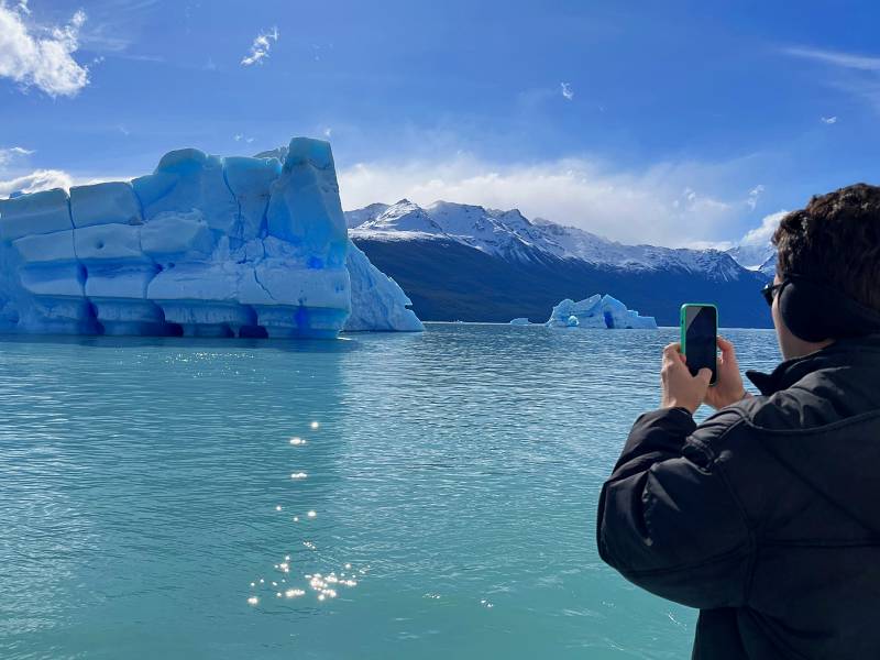 Homem segura celular e fotografa iceberg em El Calafate