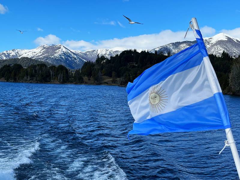 Bandeira da Argentina em barco com montanhas nevadas ao fundo em Bariloche