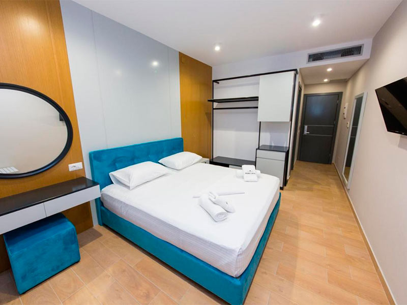 Quarto do Delight com TV, espelho redondo e cama azul