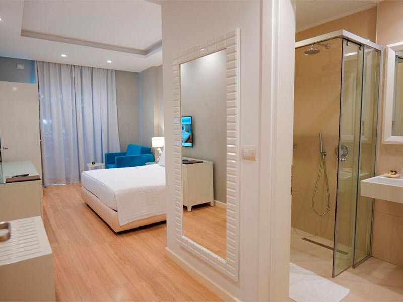 Pedaço do banheiro e do quarto do Hotel Luxury com espelho e cama de casal