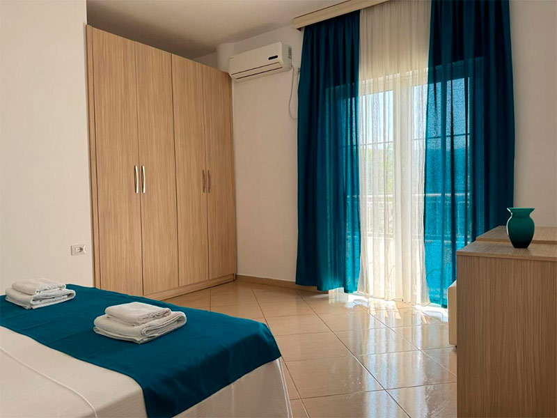 Quarto do Villa August com cama de casal, cortina azul e guarda-roupa