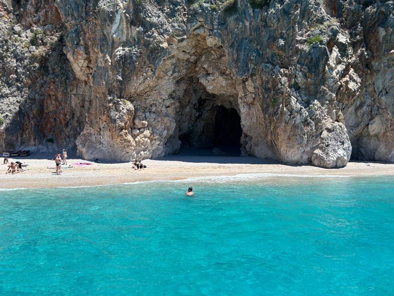 Pessoas nadam em mar azul turquesa Pigeons Cave, em Himara