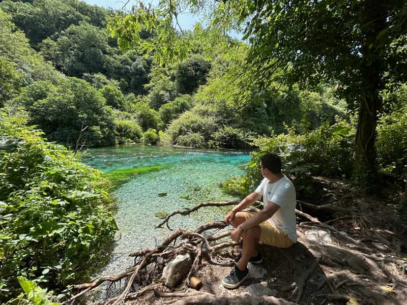 Homem sentado olhando para a água cristalina e esverdeada do Blue Eye, em Saranda