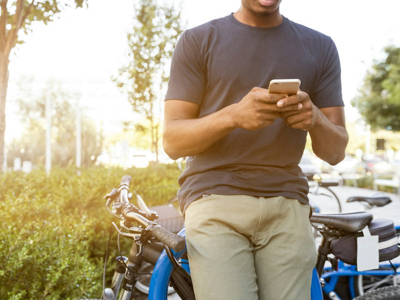 Homem segura smartphone apoiado em bicicleta em área pública