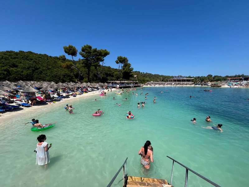 Pessoas se divertem no mar claro e esverdeado de Ksamil em dia de céu azul