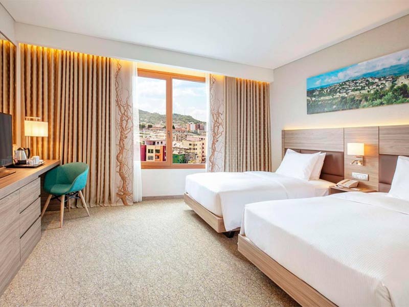 Quarto do Hilton Garden Inn, dica de onde ficar na Albânia, com duas camas e grande janela com vista de Tirana