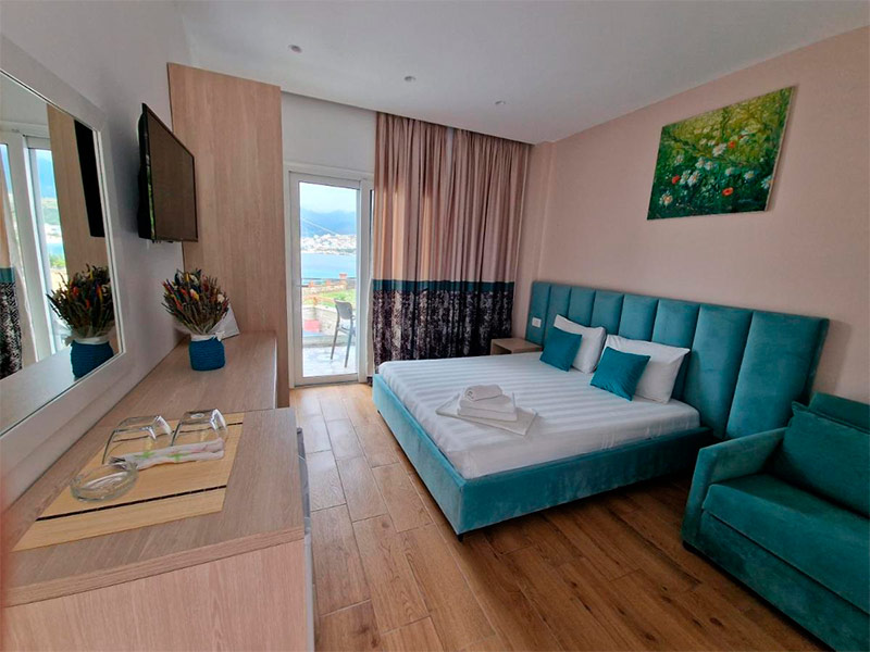 Quarto do Seaside com cama de casal com cabeceira verde, TV e varanda