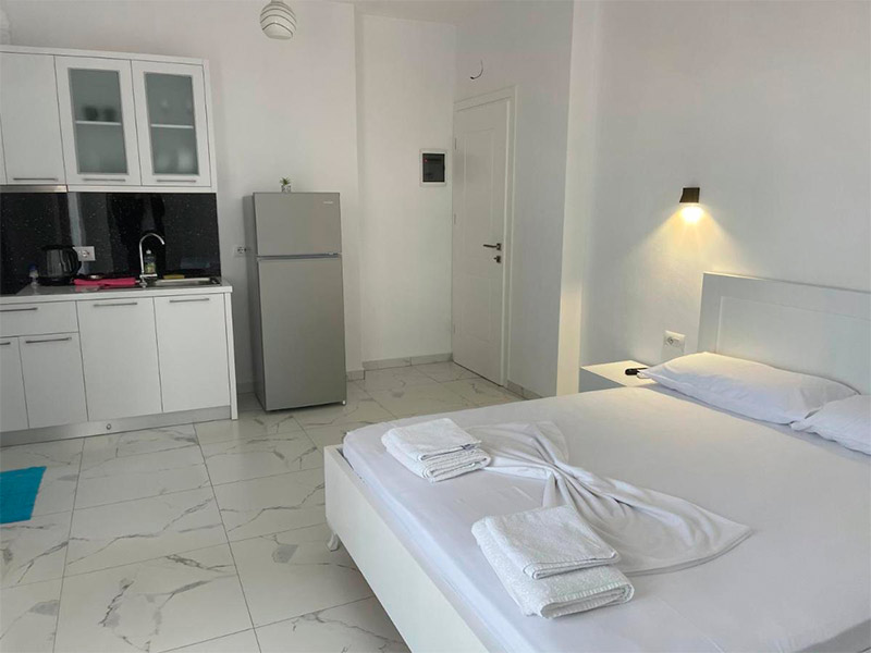 Quarto da Villa Denis com cama de casal e geladeira em decoração branca