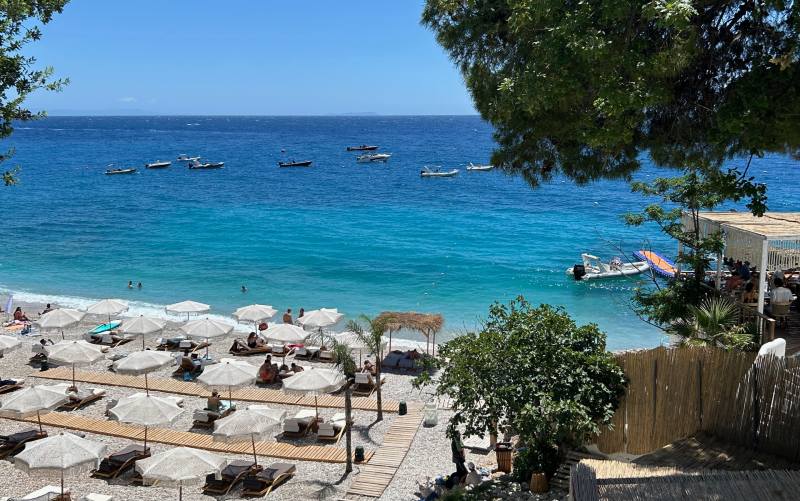 Vista da praia de Dhermi com guarda-sóis em dia de céu azul e mar claro