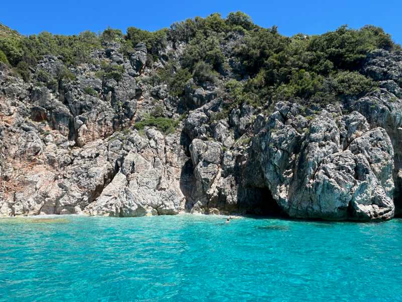 Mas azul esverdeado de praia em Himara, na Albânia, com caverna e céu azul