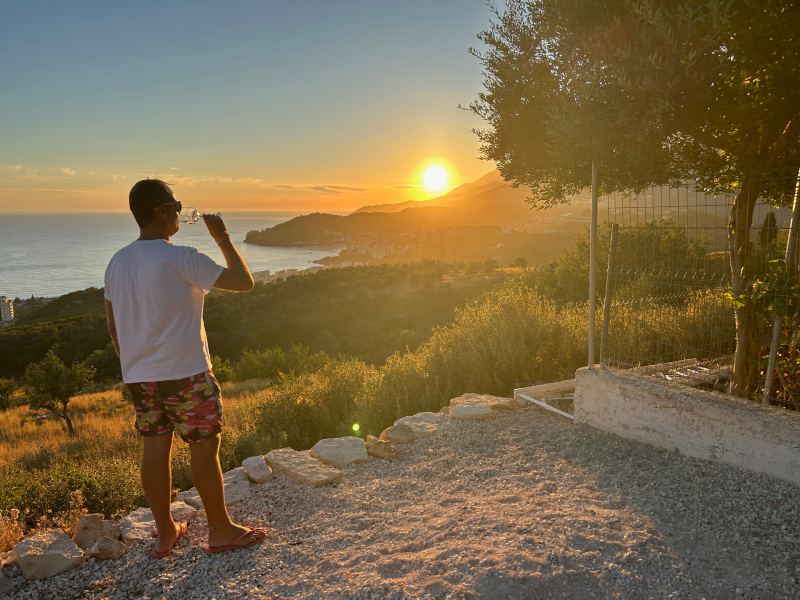 Homem toma vinho com vista do pôr do sol na primavera em Himara, dica de quando ir pra Albânia