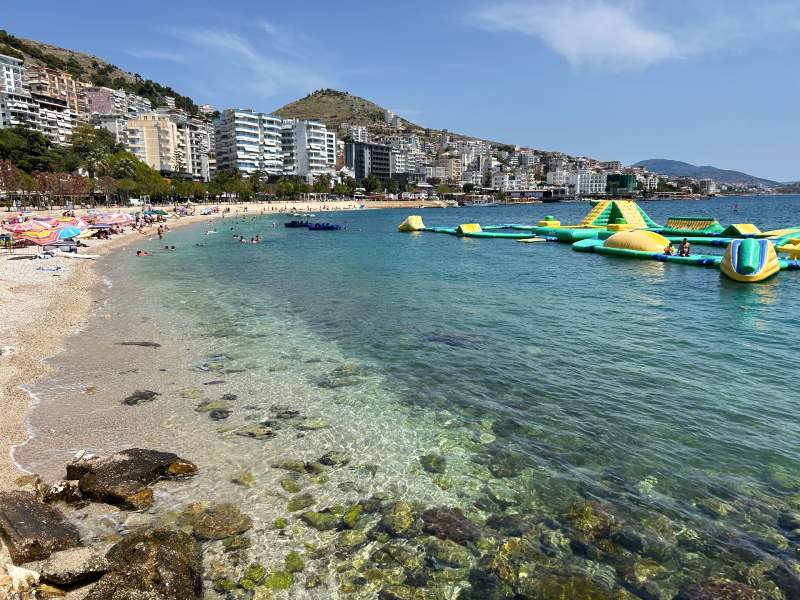 Vista da praia em Saranda com préios ao fundo em dia de céu azul