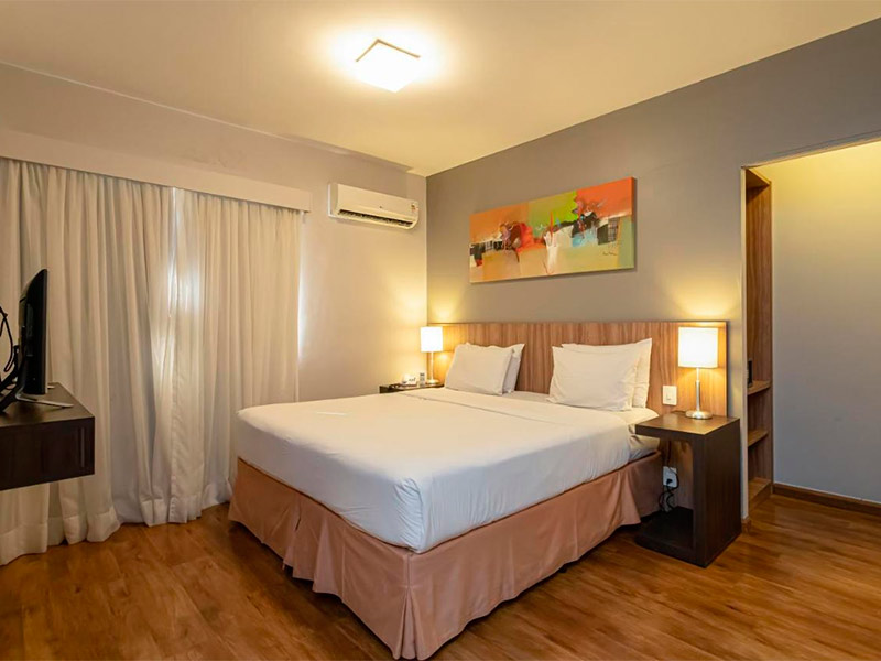 Quarto do H4 La Residence Paulista, dica entre os hotéis perto do Allianz Parque, com cama de casal, TV e quadro colorido na parede