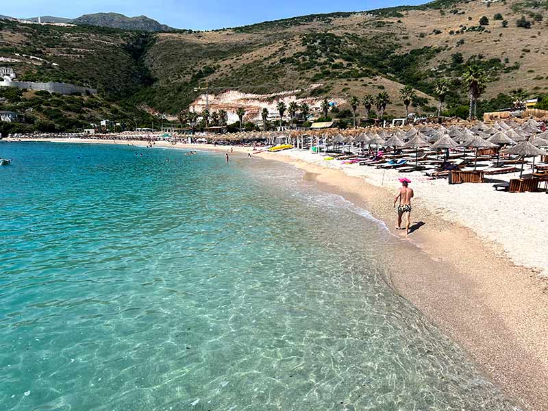 Homem caminha à beira-mar pela praia de Jale com mar cristalino