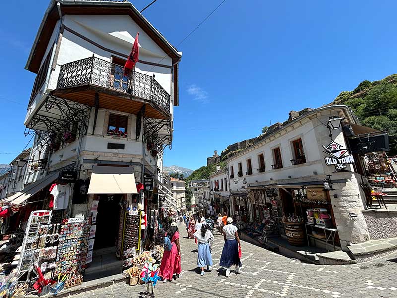 Pessoas andam pelo centro histórico de Gjirokaster, dica de o que fazer na Albânia, em dia de céu azul