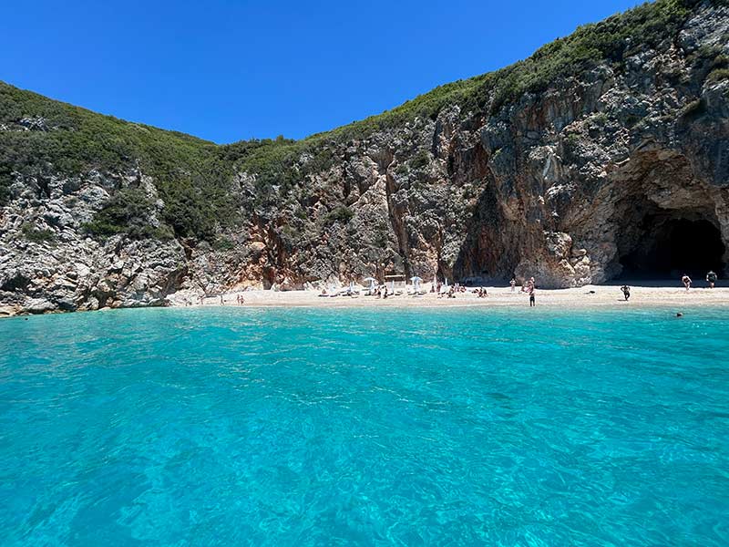 Mar esverdeado e cristalino da Pigeons Cave com areia e caverna em Himara