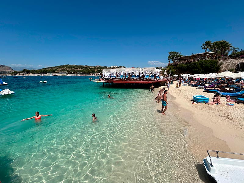 Praia em Ksamil com águas cristalinas e pessoas se divertindo no mar