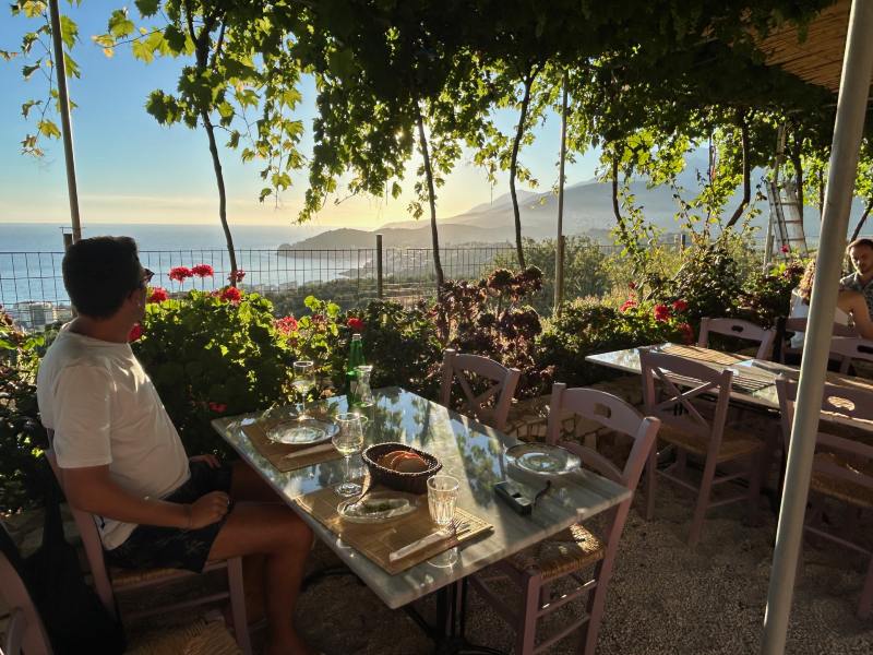 Homem sentado em restaurante Eléa com pratos típicos em Himara, na Albânia, perto do pôr do sol