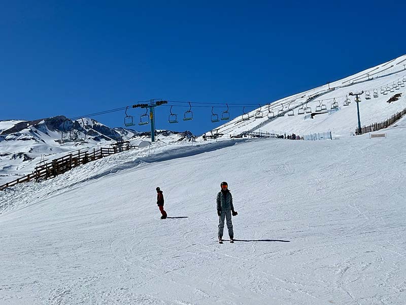 Pessoas esquiando em dia de céu azul e muita neve em pista no Chile