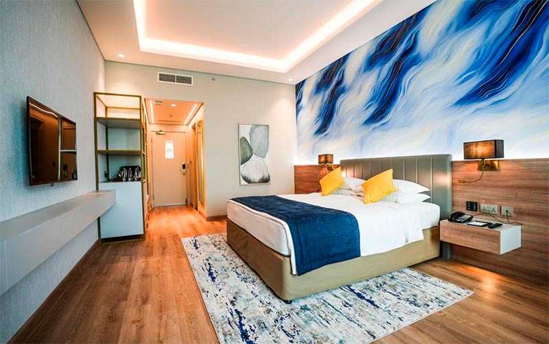 Quarto do Mövenpick Grand Al Bustan, dica de hotel no aeroporto de Dubai, com cama de casal, almofadas amarelas e quadro azul