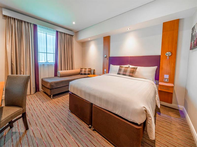 Quarto do Premier Inn, dica de hotel no aeroporto de Dubai, com cama de casal e painel roxo