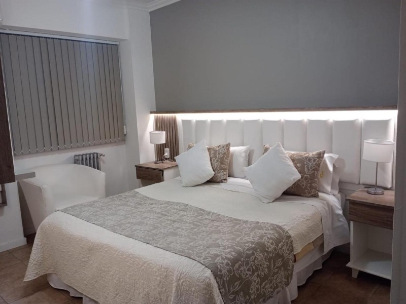 Quarto do San Martín, dica de hotel em Mendoza, com cama de casal, decoração cinza e branca e poltrona