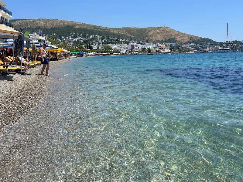 Praia central de Bodrum com mar esverdeado em dia de céu azul