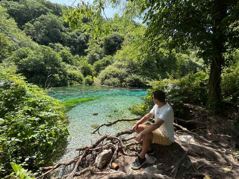 Homem sentado observa as águas cristalinas de Blue Eye, na Albânia